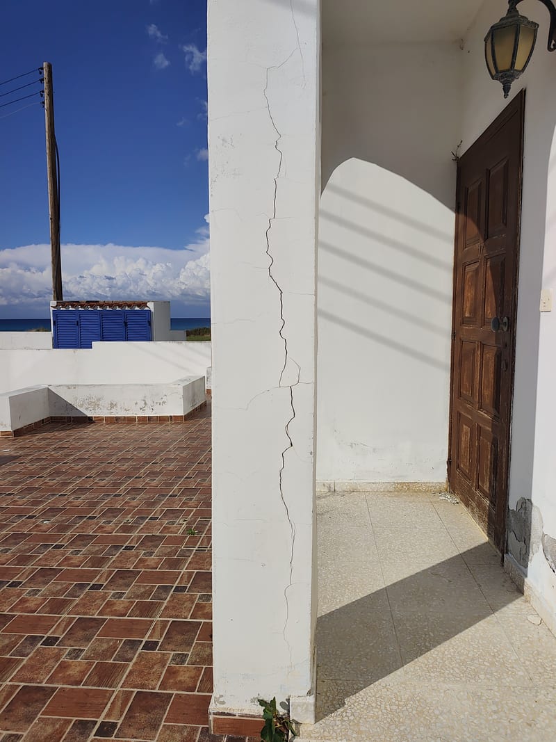 A crack running up a white wall beside a wooden front door